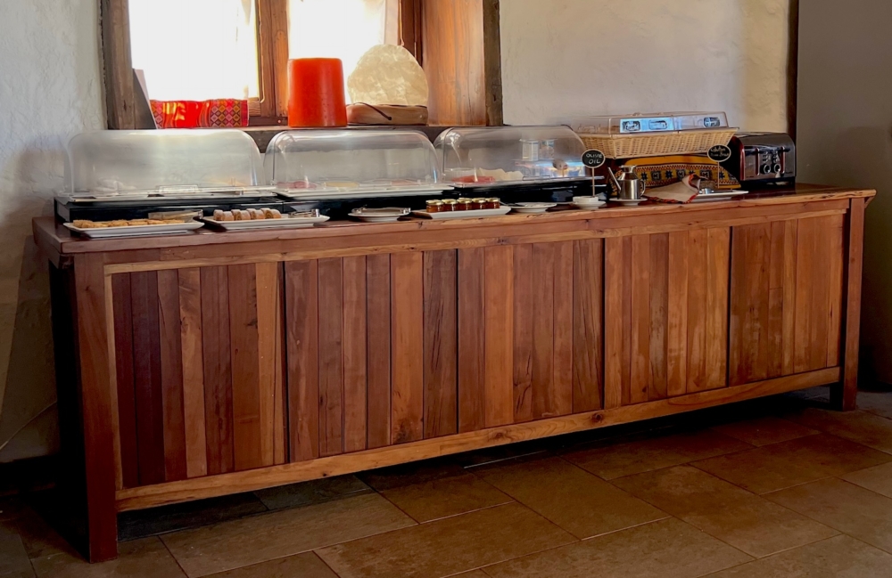 A buffet of cold breakfast items such as fruit, yogurt, cheese, and pastries. the food is on top of a long table made of wood. The table is against a wall.
