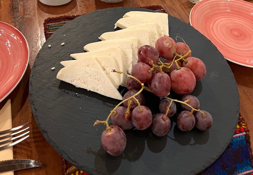 A close up of a black stone plate that is on a table. The plate is in the middle of the picture and has cheese and grapes on it. To the left and right sides of the black plate are two ceramic plates. Each of those are painted with a peach and white colored spiral. 